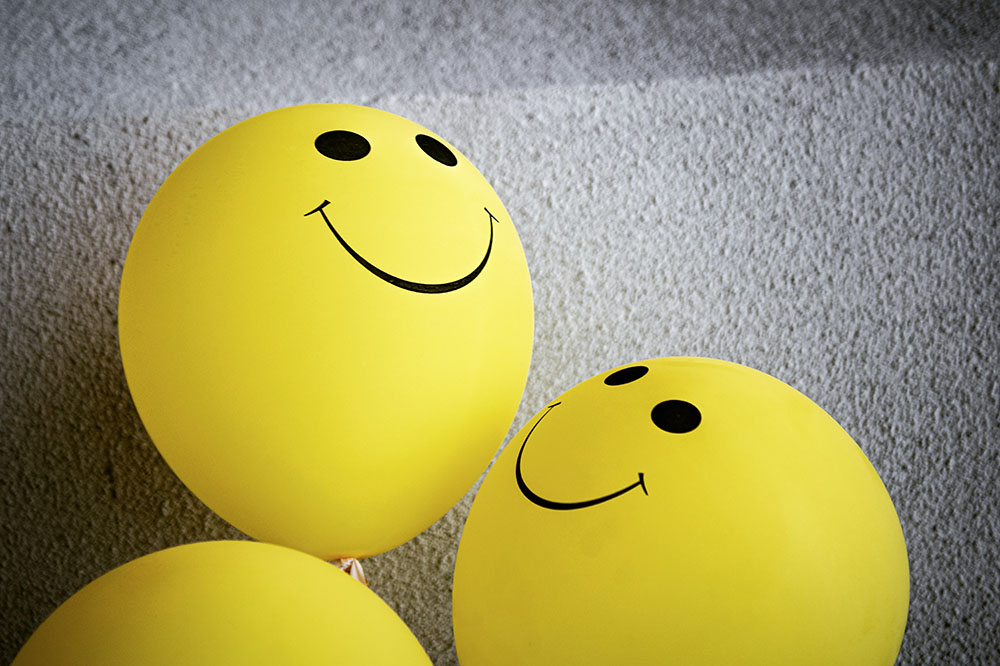 deux ballons jaunes avec dessin noir yeux et bouche smiley souriant un ballon jaune vue partielle fond béton gris clair